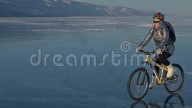 女人在冰上骑自行车。 女孩穿着银色的羽绒服，背包和头盔。 骑自行车的人